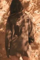 Camisa oversize marrón de gasa, con cuello solapa, manga larga de hombro caído con puño ancho, bolsillo aplicado en el frente y cierre frontal con botones.