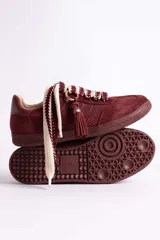 Zapatillas urbanas color tostado con textura geométrica en el cuerpo y detalles de gamuza en la puntera y laterales. Presentan un diseño distintivo con cordones anchos tejidos en tonos tostado y blanco, y un accesorio metálico con borla de gamuza en el empeine.