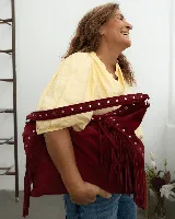 Cartera estilo hobo de gamuza color bordó, con flecos laterales y asa ancha decorada con tachas metálicas plateadas.