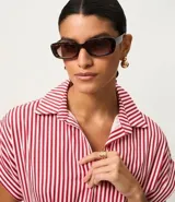 Vestido largo estilo chemise con estampado de rayas rojas y blancas, cuello clásico, cierre frontal con botones y mangas cortas amplias. Incluye un cinto desmontable para ajustar en la cintura.