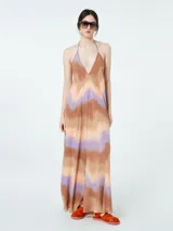 Vestido largo con estampado tie-dye en tonos marrones, naranjas y lilas. Tiene escote halter y espalda descubierta.
