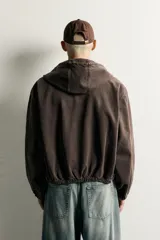 Cazadora de denim de algodón color negro con efecto lavado, de corte relaxed fit, manga larga y capucha. Cuenta con cierre frontal de cremallera, bolsillos frontales tipo canguro y acabados con elástico en puños y cintura.
