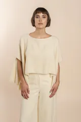 Poncho color beige con diseño a cuadros, cuello bote y terminaciones desflecadas. Tiene aberturas para los brazos en los laterales y detalles en cuero.