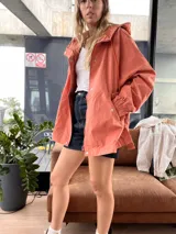 Campera color ladrillo con capucha, cierre frontal con cremallera y broches a presión, bolsillos laterales con solapa y puños elásticos.