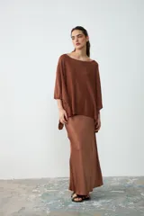 Poncho corto de tejido de punto color habano con sutiles destellos brillantes, de cuello bote y mangas amplias.