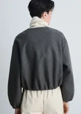Chaqueta tipo bomber de color gris oscuro, con cuello redondo, cierre frontal de cremallera y diseño oversize. Presenta mangas largas con puños elásticos fruncidos y detalle fruncido en el bajo, además de dos bolsillos laterales.