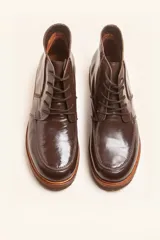 Bota acordonada de cuero vacuno con acabado charol color suela, con suela de goma tipo crepe y costuras reforzadas.