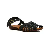 Sandalia plana de mujer, color negro, con puntera cerrada tejida con tiras cruzadas y tira de ajuste con hebilla metálica en el tobillo. La suela es de color marrón.
