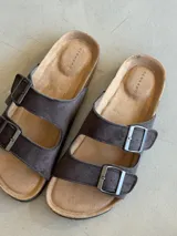 Sandalias de cuero sintético color marrón con doble tira y hebillas metálicas ajustables.