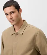 Sobrecamisa de sarga de algodón en color beige, de corte amplio y estructurado, con cuello camisero, mangas largas, cierre frontal de botones ocultos y grandes bolsillos frontales con solapa.