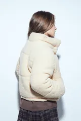 Campera puffer de corderito negro con cuello alto y diseño oversized. Presenta una textura tipo teddy, cierre frontal y corte a la cintura.