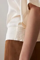 Blusa color beige de tela satinada, con escote barco y mangas cortas.