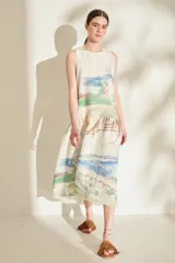 Vestido midi sin mangas, de corte recto y suelto con volante fruncido en la parte inferior. Presenta un estampado artístico tipo acuarela con paisajes en tonos claros.