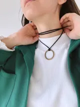 Gargantilla tipo choker de cordón negro con dije circular metálico en tono bronce.