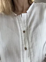 Camisa de manga larga de bambula de algodón, color blanco, con cuello mao, apliques de encaje en la pechera y botones frontales de coco. Diseño holgado.