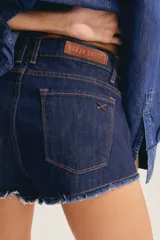 Short de denim azul oscuro con tiro bajo y ruedo deshilachado. Cuenta con bolsillos delanteros, cierre frontal con botón metálico personalizado y costuras en contraste.