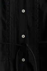 Vestido largo negro de popelina de algodón con alforzas, inserciones de encaje, manga corta abullonada, cuello camisero, botonadura frontal y cinturón fino para atar en la cintura.