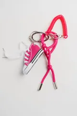 Llavero con dije de zapatilla deportiva en miniatura color fucsia con cordones blancos, argolla metálica, espiral de plástico fucsia y cordón de seda fucsia con terminales metálicas.