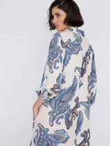 Vestido camisero largo con estampado paisley en tonos celeste, azul y marrón. Tiene cuello camisero, mangas largas con puños abotonados, cierre frontal con botones y un bolsillo en el pecho.