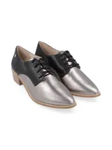 Zapato acordonado de estilo oxford con diseño bicolor. Presenta una puntera y lateral en cuero metalizado plateado, mientras que la parte trasera y el área de los cordones están confeccionados en cuero con textura de reptil en color negro. Incluye un taco bajo de madera y suela a tono.