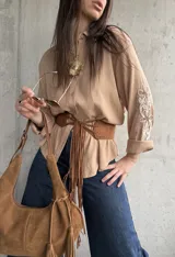 Camisa camel de mangas largas con bordados florales blancos en las mangas, cuello camisero y cierre frontal de botones.