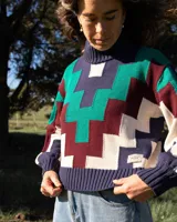 Sweater de cuello alto tejido con diseño geométrico en zigzag multicolor, incluyendo tonos azul marino, verde, bordó y crema. Presenta puños y ruedo acanalados.