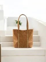 Bolso tipo tote de cuero color marrón claro con costuras verticales decorativas en hilo color crudo.