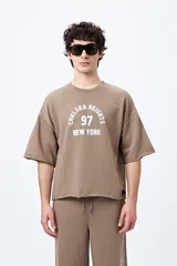 Buzo color marrón con estampado frontal blanco que dice 'Chelsea Heights 97 New York', corte holgado y mangas cortas.