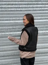 Chaleco gamulán corto marrón de efecto cuero, con interior y detalles de corderito sintético a tono. Cuenta con cuello alto y tiras laterales con hebilla para ajustar la cintura.