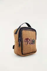 Bolso tote de mano color tostado, tejido con textura tipo mimbre o rafia, con bordes y detalles en azul marino. Cuenta con un asa superior corta, cierre con cremallera y un bordado frontal con la palabra "Rio" que incluye motivos tropicales de una palmera y un tucán.