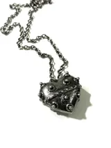 Collar de acero quirúrgico con dije de corazón en aleación pesada de metal plateado envejecido, decorado con tachas y detalles texturizados.