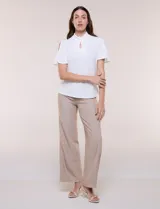 Blusa blanca de corte recto con cuello alto torzado, abertura frontal en gota y mangas cortas con aberturas sobre los hombros.
