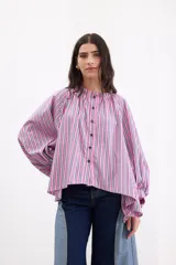 Camisa holgada de popelina de algodón con rayas verticales en tonos rosado, gris y blanco. Presenta cuello alto con volado, hombros caídos, mangas anchas abullonadas y cierre frontal con botones.