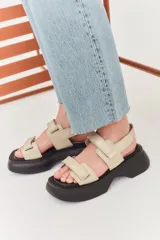 Sandalias de plataforma con suela de goma negra y tiras de cuero sintético color beige con cierre de velcro ajustable.