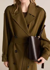 Trench coat de corte oversize y diseño largo en color verde oliva. Presenta cierre de doble botonadura, cuello con solapas de muesca, trabillas en hombros y mangas, y cinturón desmontable a tono. Incluye forro interior y abertura posterior en el bajo.