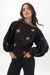 Blusa negra de algodón con mangas largas abullonadas y escote a la base. Presenta un bordado artesanal con motivos marinos como estrellas de mar, corales y peces en colores vibrantes.