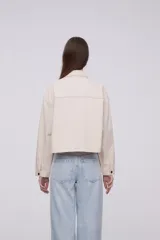 Chaqueta de algodón color beige, con diseño holgado, cuello tipo camisa, cierre frontal con botones metálicos y bolsillos frontales con solapa.