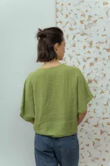 Blusa de lino color fucsia, con escote en V y manga corta amplia. Presenta un detalle de botón decorativo dorado en el centro del escote.