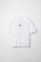 Remera blanca de corte oversize con cuello redondo y mangas cortas. Presenta un pequeño bordado en el pecho con texto en color oscuro.
