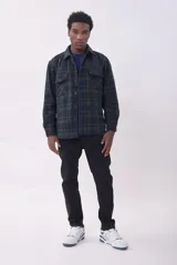 Campera tipo camisa de franela con estampado de cuadros en tonos verde y azul marino. Presenta cierre frontal con botones, cuello clásico y dos bolsillos frontales con solapa en el pecho.