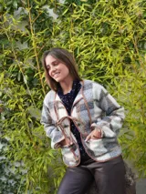 Chaqueta corta con estampado a cuadros en tonos negro, gris y marrón, con ribetes en marrón y cierre frontal con lazos.