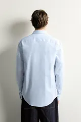 Camisa slim fit de algodón color celeste con sutil patrón de cuadros, cuello clásico y manga larga con puños abotonados.