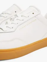 Zapatillas de cuero napa color blanco con suela de goma color caramelo. Presentan un diseño clásico de corte bajo con cordones, logo metalizado de Tommy Hilfiger en relieve en el lateral y la lengüeta, y logo en el talón.