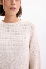 Sweater de punto fantasía color crudo, de corte holgado, con cuello redondo y mangas largas.
