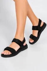 Sandalias negras de tiras ajustables con cierre de velcro, suela plana y diseño cómodo para uso diario.