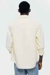 Camisa H&M de algodón Oxford en color amarillo claro, con cuello americano, bolsillo en el pecho y cierre frontal con botones.