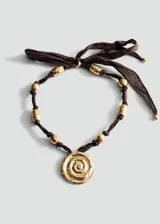 Collar con cinta marrón ajustable en la parte posterior, abalorios dorados texturizados a lo largo de la tira y un dije circular central dorado con diseño de espiral en relieve y pequeños cristales incrustados.