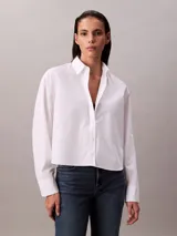 Camisa blanca de algodón y elastano, con cuello clásico de punta, cierre frontal con botones y mangas largas con puños abotonados.