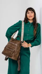 Mochila de símil cuero color marrón con apertura superior y tres bolsillos frontales con cierres metálicos. Cuenta con bolsillos laterales y una correa de galón con diseño geométrico, regulable y extraíble, que permite su uso como bandolera.