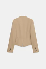 Blazer entallado de sarga color beige con cuello subido y escote en pico. Presenta manga larga con hombreras, detalle de botones metálicos decorativos en el frente y cierre frontal con gancho metálico. Incluye falsos bolsillos de vivo y abertura en la espalda.
